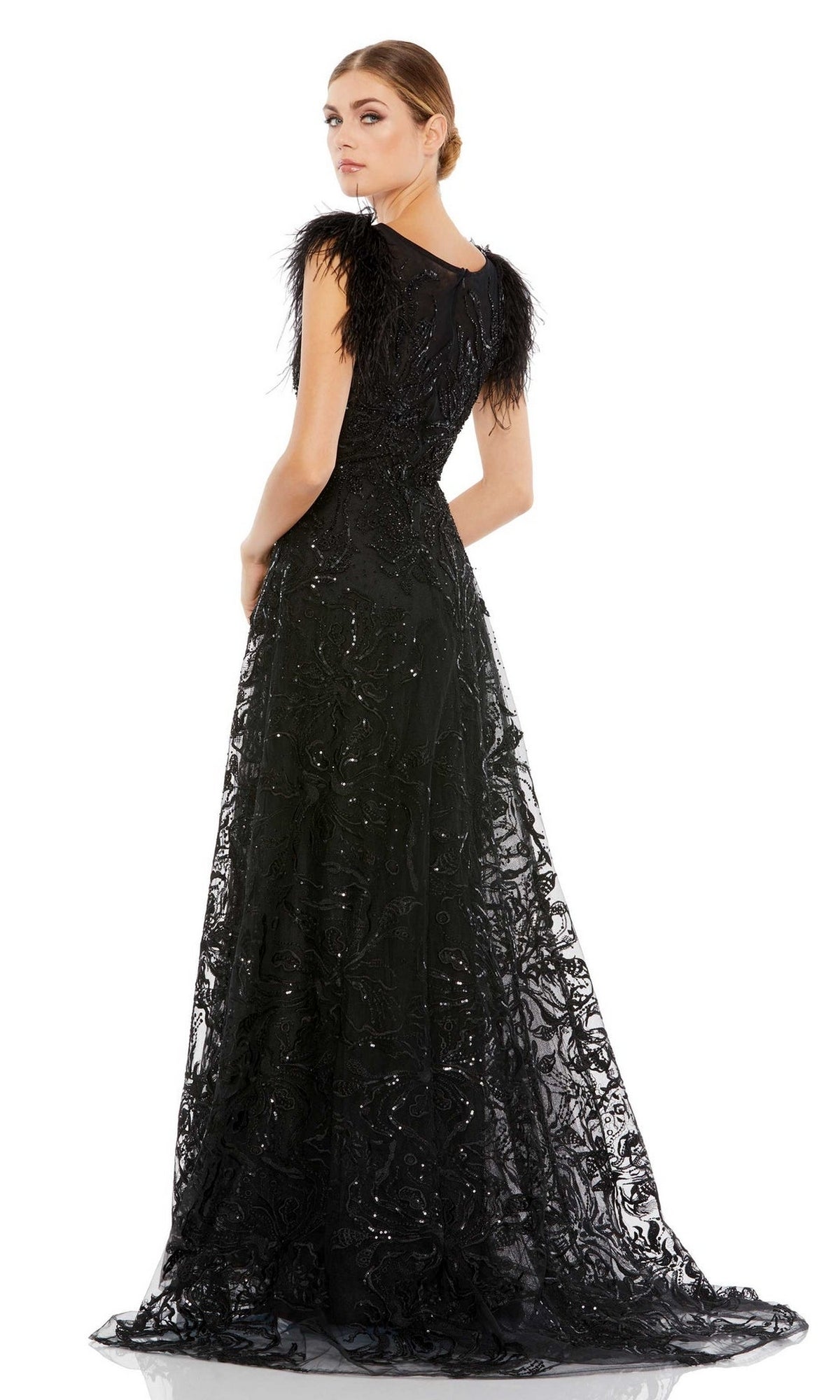 Woman wearing the Mac Duggal 20296 Feather Long Black Formal Dress, featuring feathered shoulders and an embroidered lace overlay, stands looking over her shoulder.